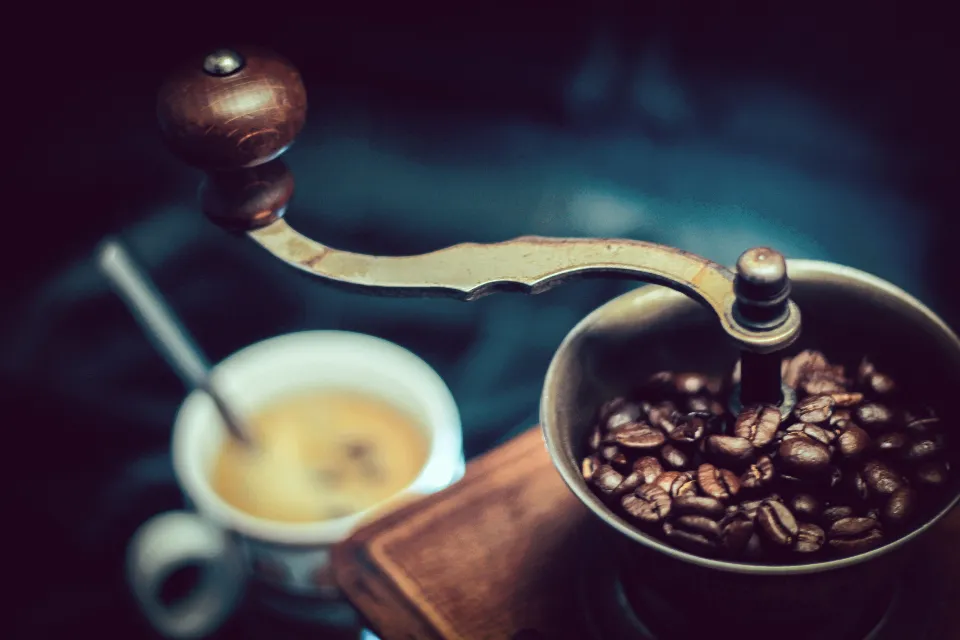 Antique hand-crank coffee grinder with coffee beans and a cup